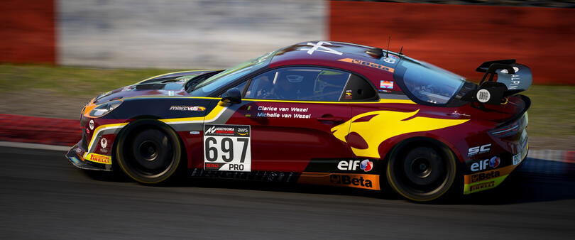 Picture of an Alpine A110 GT4 sporting a Marc VDS livery. It is candy red with yellow and black accents, with the Marc VDS lion logo on the rear quarter panels.